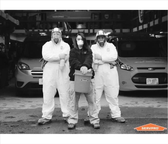 A photo of 3 SERVPRO technicians, one standing with a bucket and two in full protective suits