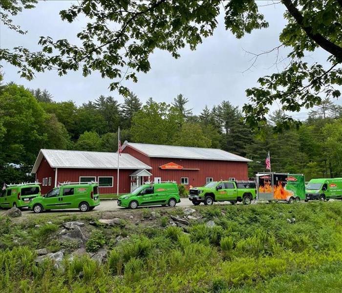 Row of green trucks arranged in front of large red building.
