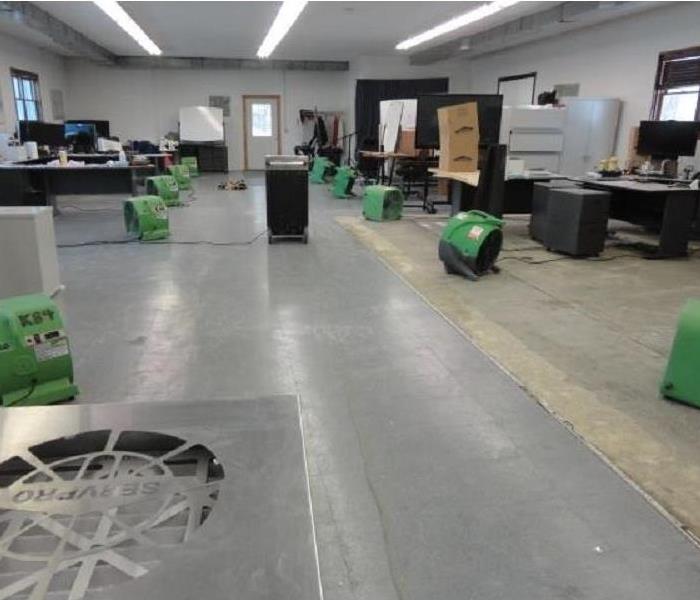 Commercial office space with several large green fans and dehumidifiers installed for drying.
