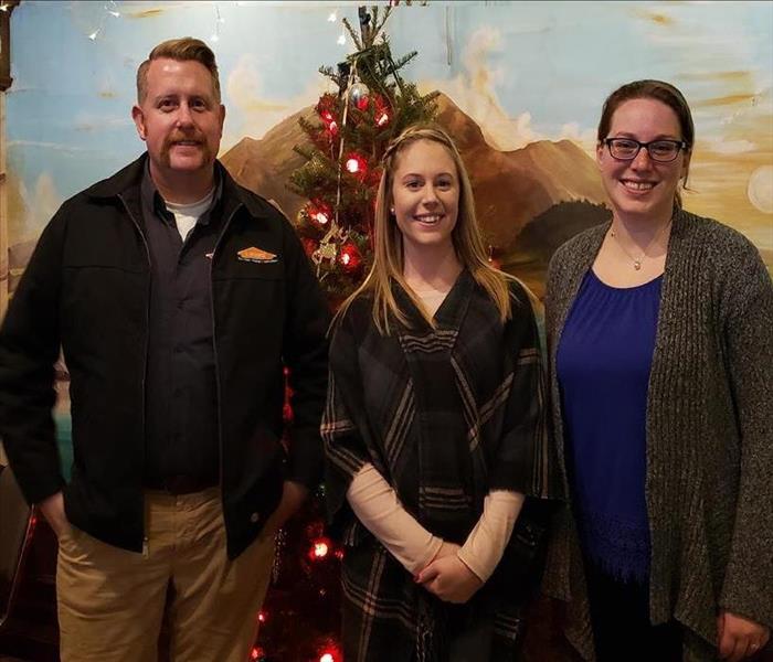 a man and two women standing in front of a Christmas tree and a wall mural smiling
